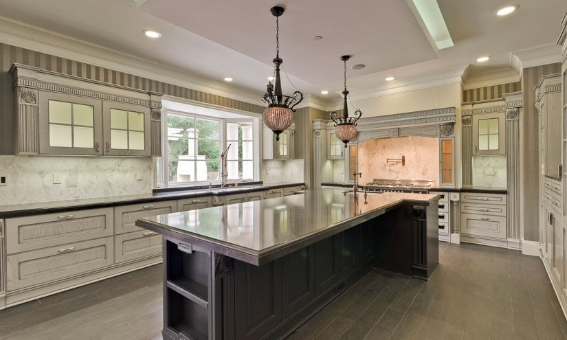 This traditional kitchen uses multiple layers of lighting: Recessed cans and up lighting over the island for ambient light; under cabinet lighting and task lighting over the gas range; pendants over the island for ambiance; decorative in-cabinet lights; and large windows for natural light.