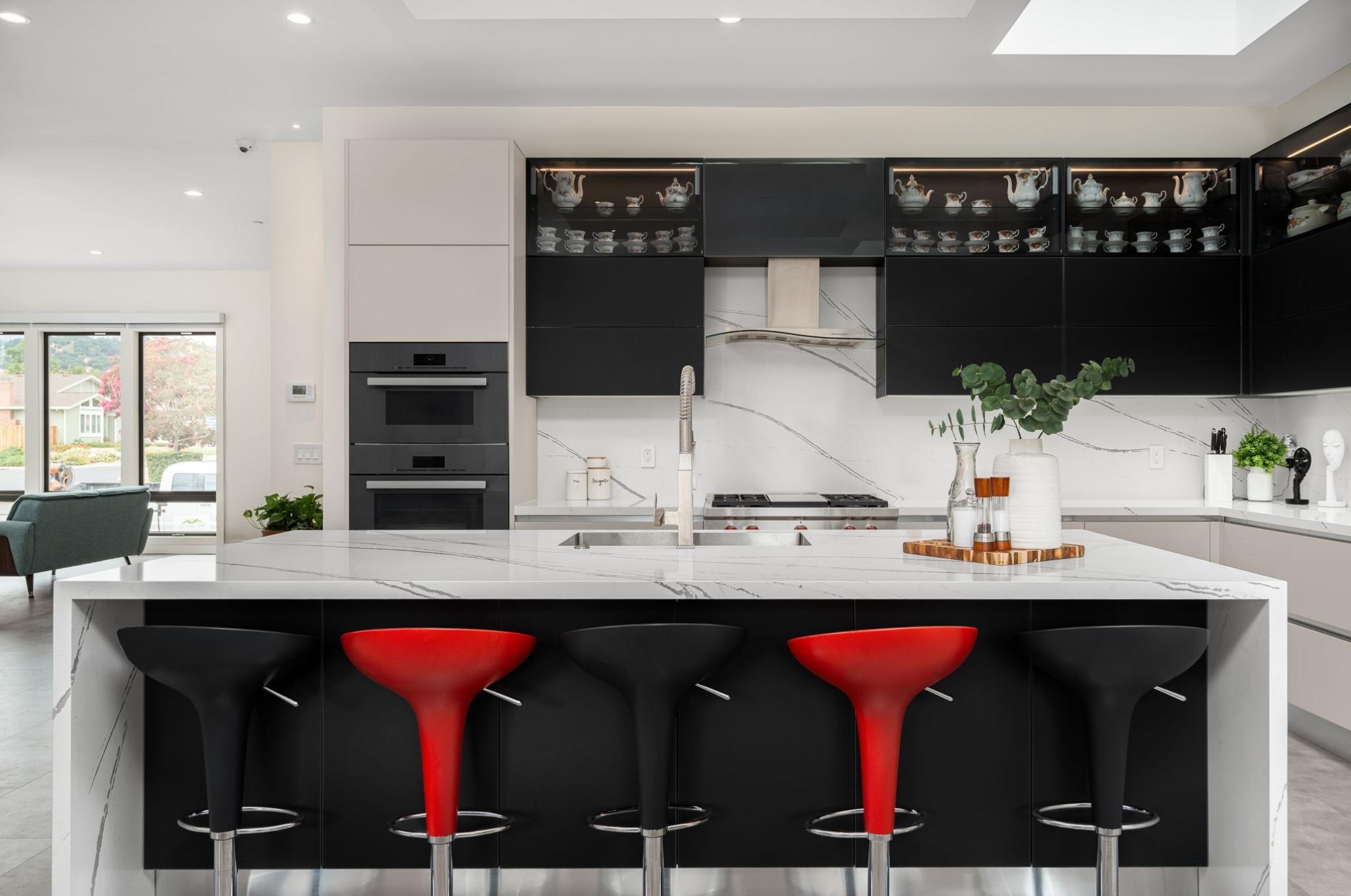 Modern black and white kitchen in Cupertino with a waterfall quartz island and bold red bar stools designed by European Cabinets & Design Studios.