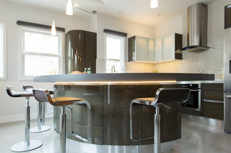 Kitchen with a curved dark wood-grain island, under-cabinet lighting and windows on two walls.
