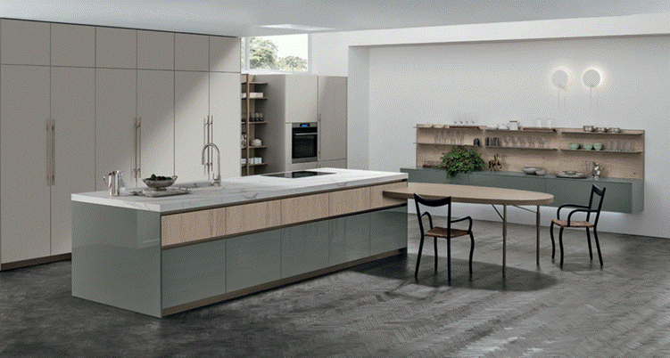 Kitchen island with gloss grey-green lower fronts and light wood drawer fronts, with tall light-colored cabinetry behind.